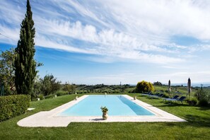 Una piscina rectangular con un cielo azul despejado y colinas lejanas al fondo.