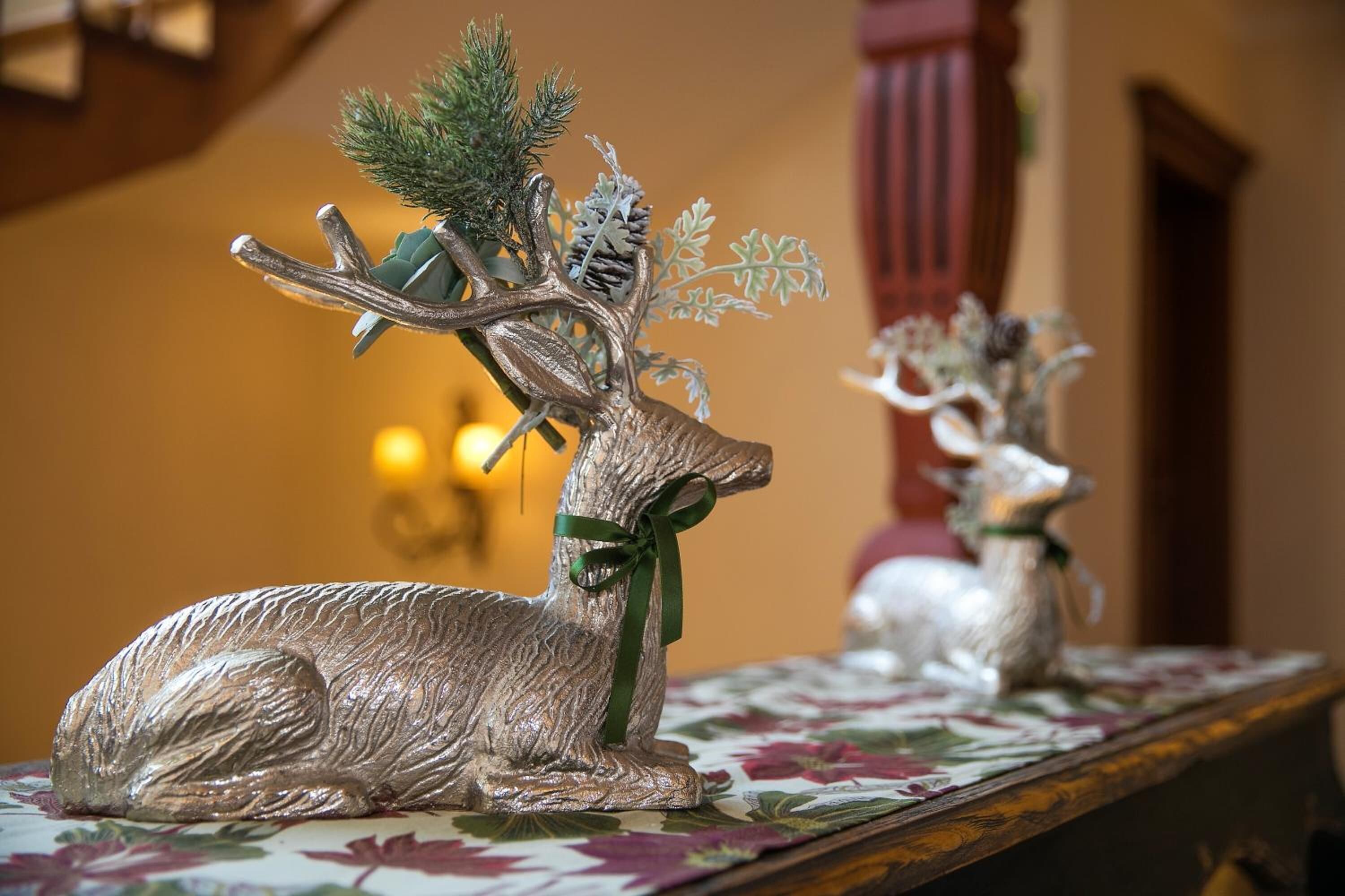 A silver deer figurine with antlers and a green ribbon on a floral tablecloth.