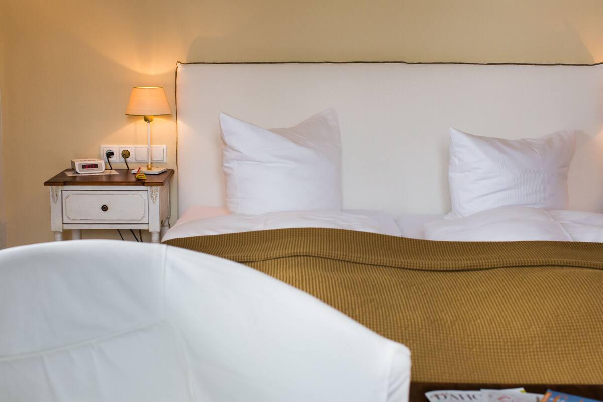 Ein Hotelzimmer mit einem Bett, einem Nachttisch mit Lampe und einem kleinen Tisch mit einer Uhr.