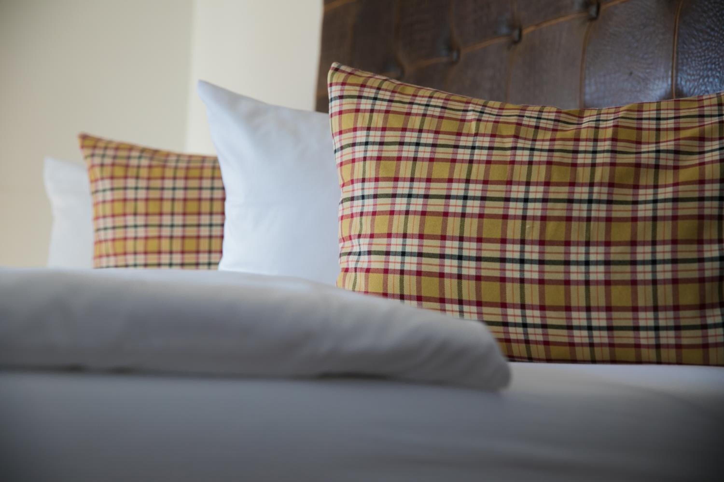 Una cama con almohadas blancas y de cuadros, un cabecero de madera y una colcha blanca.