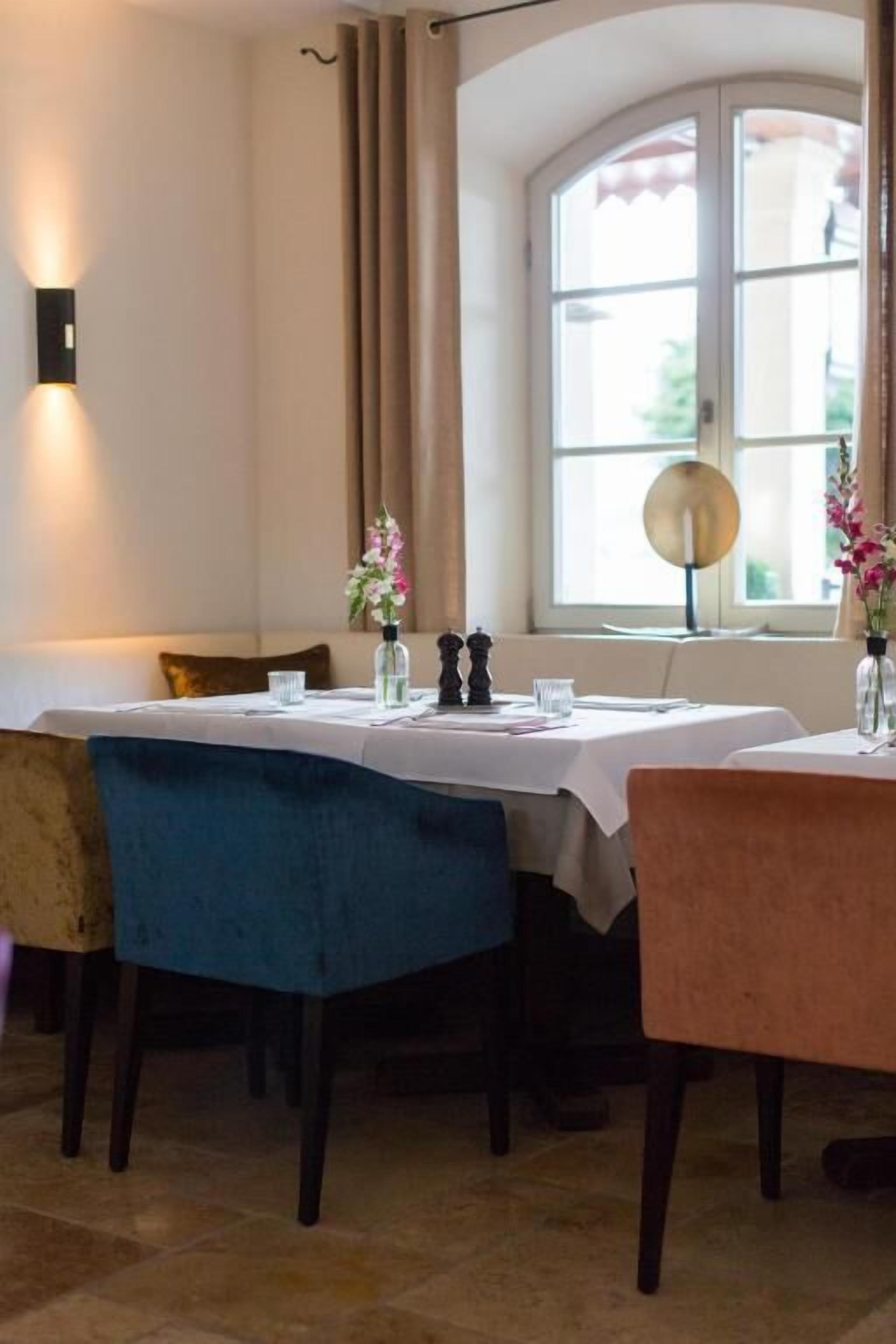 A dining area with a table set for two, a lamp, and a window with curtains.