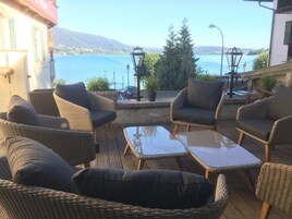 Terraza con mobiliario de mimbre y mesas de vidrio, con vista a un lago y montañas.
