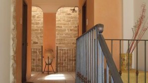A hallway with a stone wall, a metal railing, and a door leading to a room. - Sikania Suite (Pozzallo)