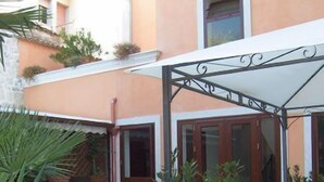 A courtyard with potted plants, a covered seating area, and a building with a tiled floor. - Sikania Suite (Pozzallo)