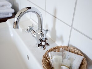 A bathroom with a chrome faucet, a white sink, and a wicker basket containing toiletries.