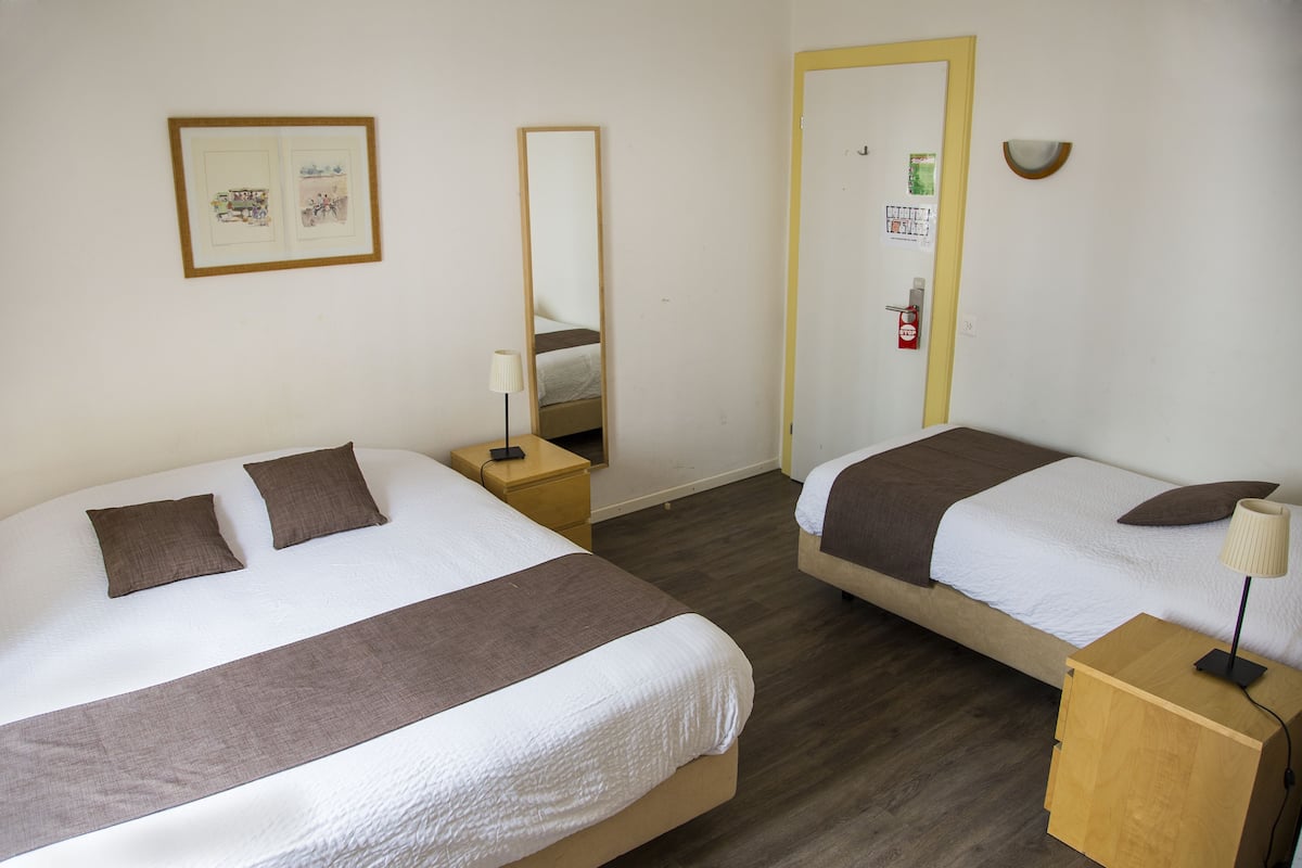 A hotel room with two beds, a bedside table with a lamp, a mirror, and a framed picture on the wall.