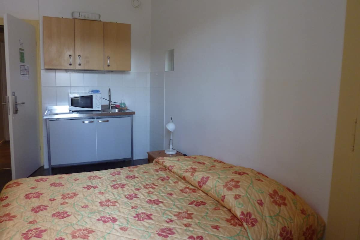 A small room with a bed, a kitchenette, and a door.