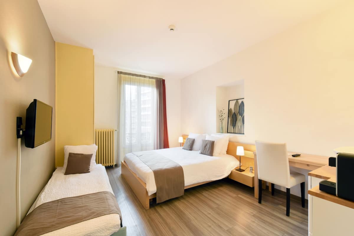 A hotel room with two single beds, a desk, a chair, a TV, and a window with curtains.
