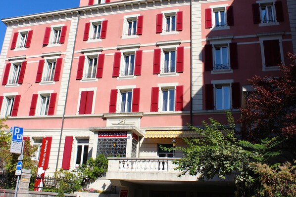 A multi-story building with red shutters, a sign for 'Hôtel du Marché', and a parking sign.