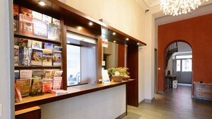 A hotel reception desk with a book display, a sign indicating the hotel, and a staircase leading to the upper floor. - Hotel du Marche (Lausanne)