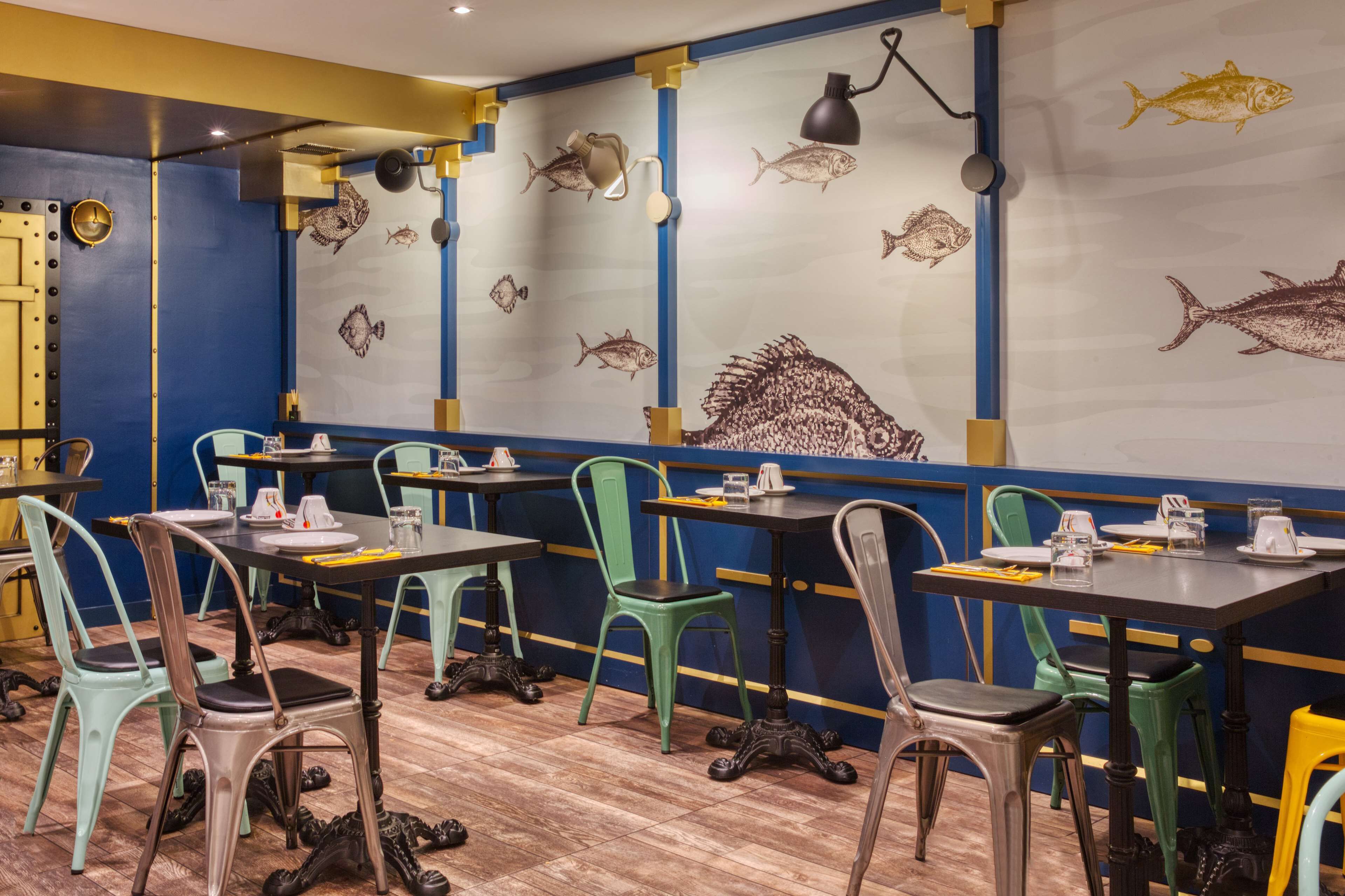 Un restaurante con mesas y sillas, una pared decorada con ilustraciones de peces y un suelo de madera.
