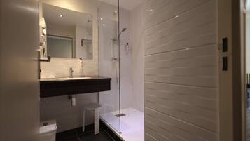 Une salle de bain moderne avec une douche à l’italienne en verre, un lavabo sur un plan de toilette foncé et des toilettes blanches.