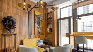 A cozy room with a wooden wall, a yellow sofa, two grey armchairs, a small table, and a bookshelf. - Best Western Hotel Graslin (Nantes)
