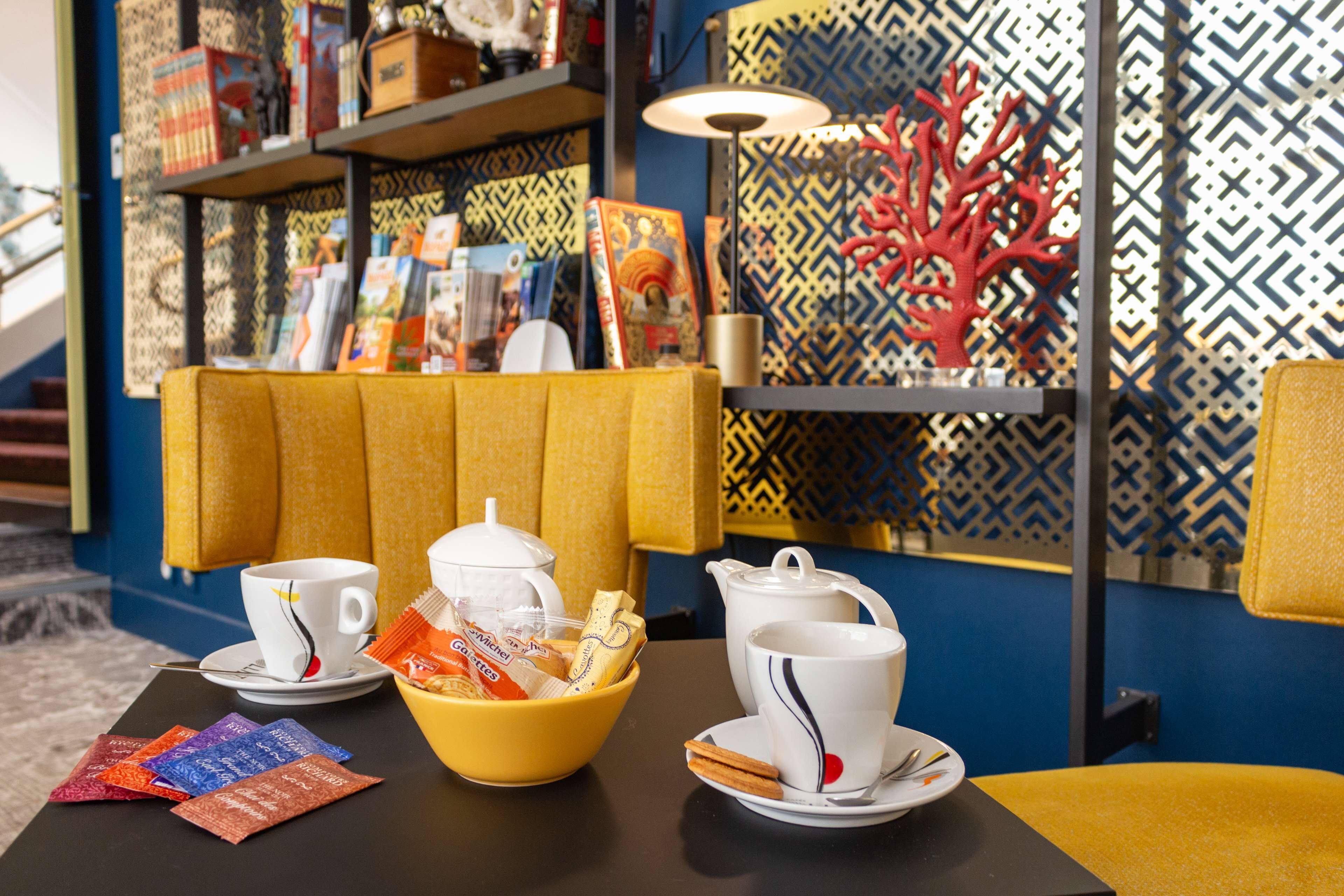 A breakfast setup with a yellow table, white cups, a teapot, and a bowl of snacks.