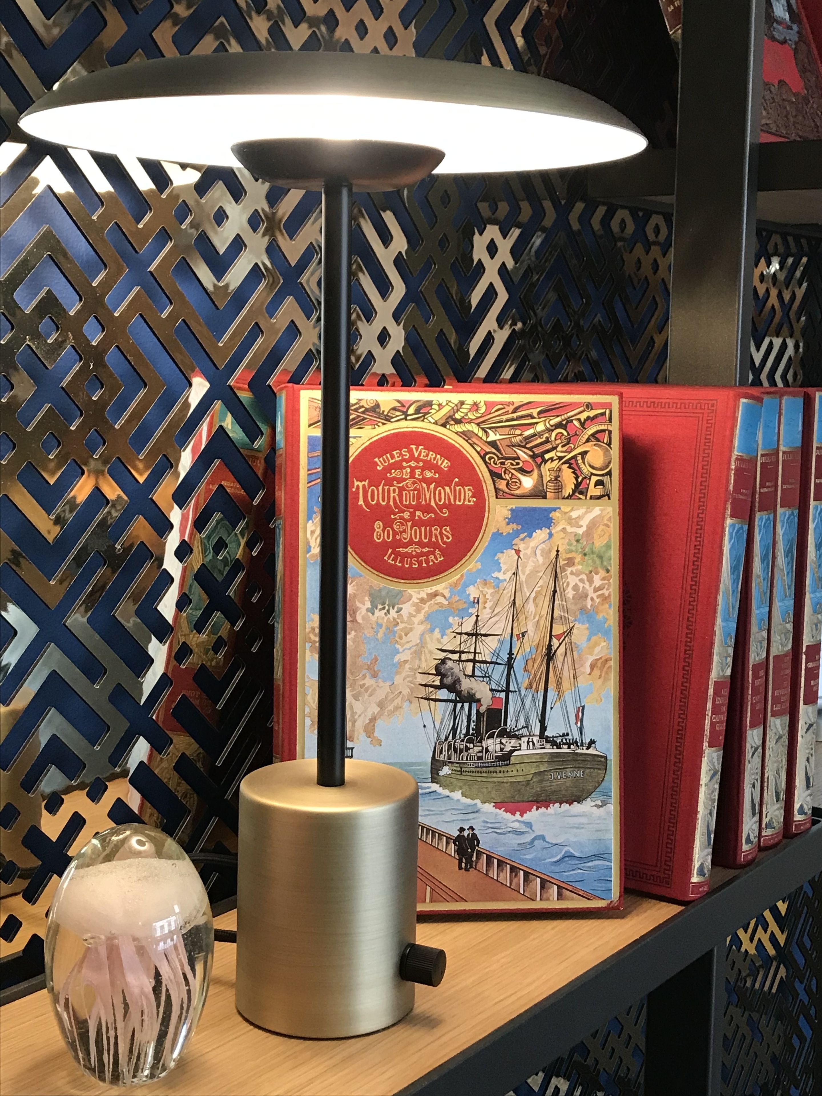 A table with a lamp, a decorative glass object, and a book titled 'Jules Verne Tour du Monde'.