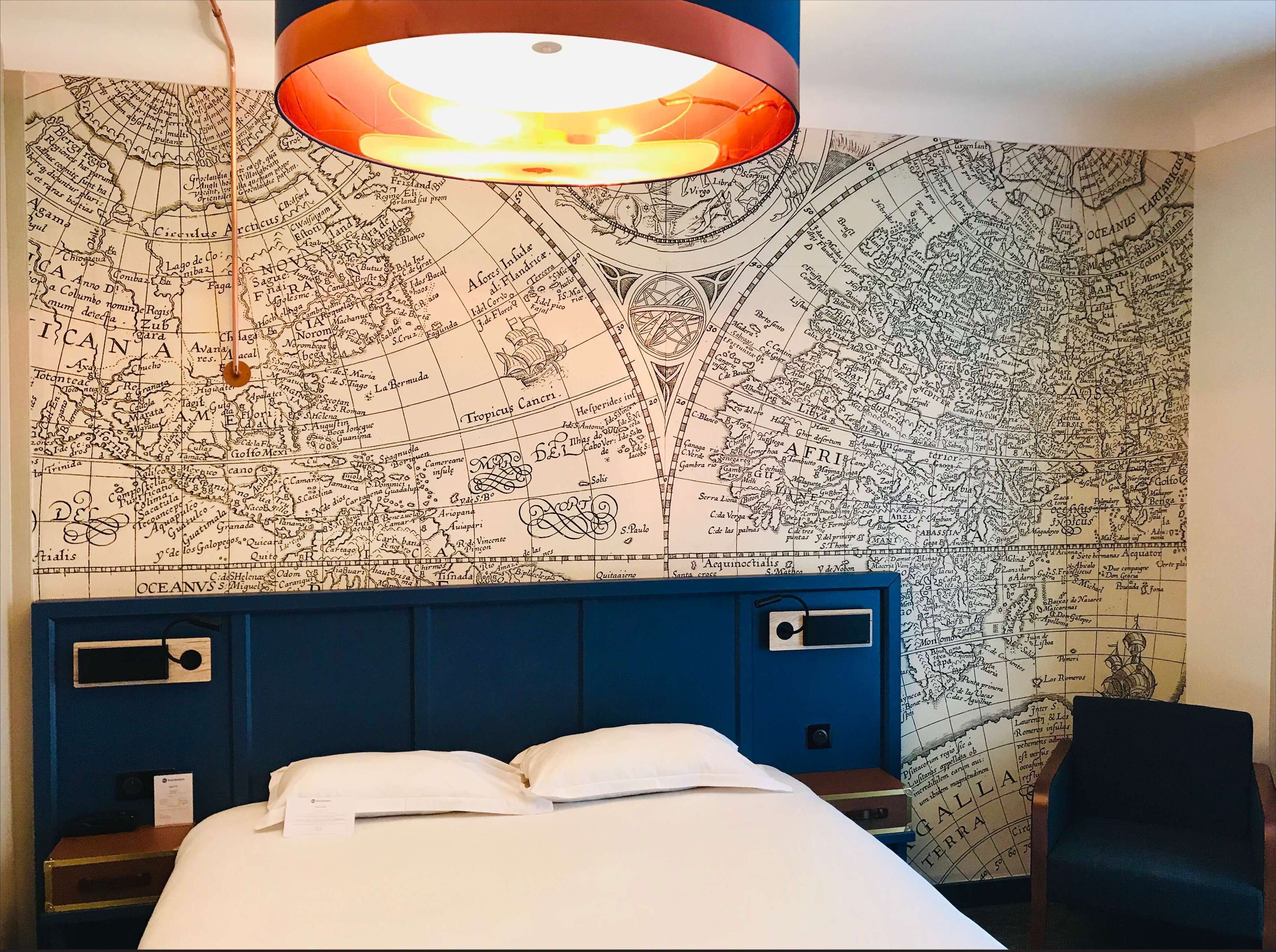 A hotel room with a large bed, a blue headboard, and a wall map.