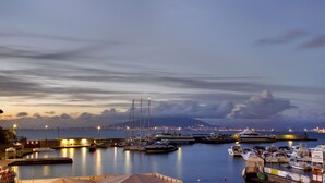 Un port esportiu amb vaixells amarrats, una muntanya al fons i un paisatge urbà a la distància.
