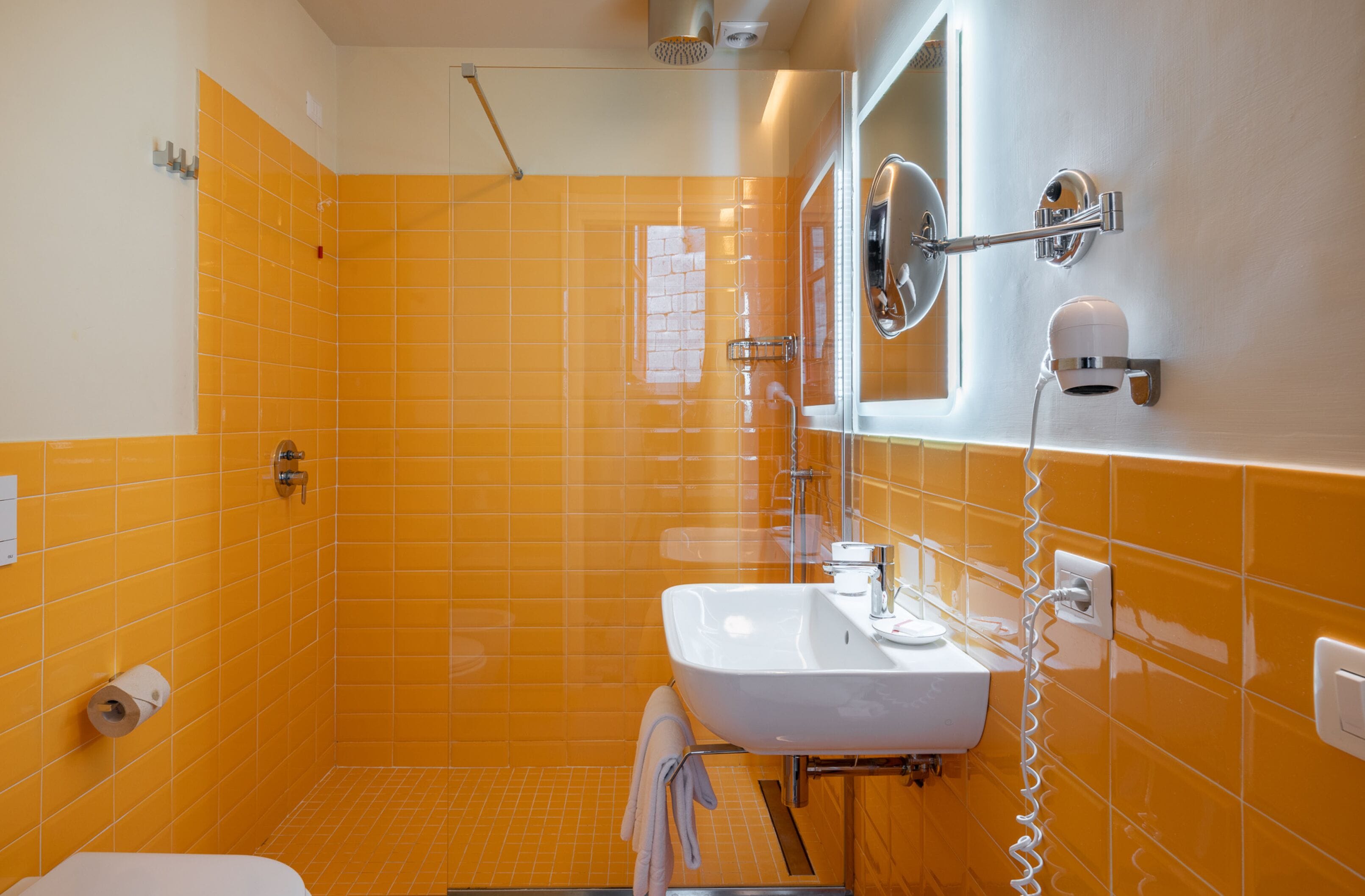Un baño con paredes de azulejos anaranjados, un lavamanos blanco, un espejo y una toalla colgada en la pared.