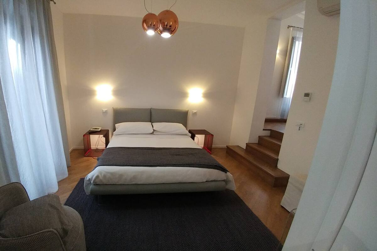 A bedroom with a bed, bedside tables, a chair, and a staircase.