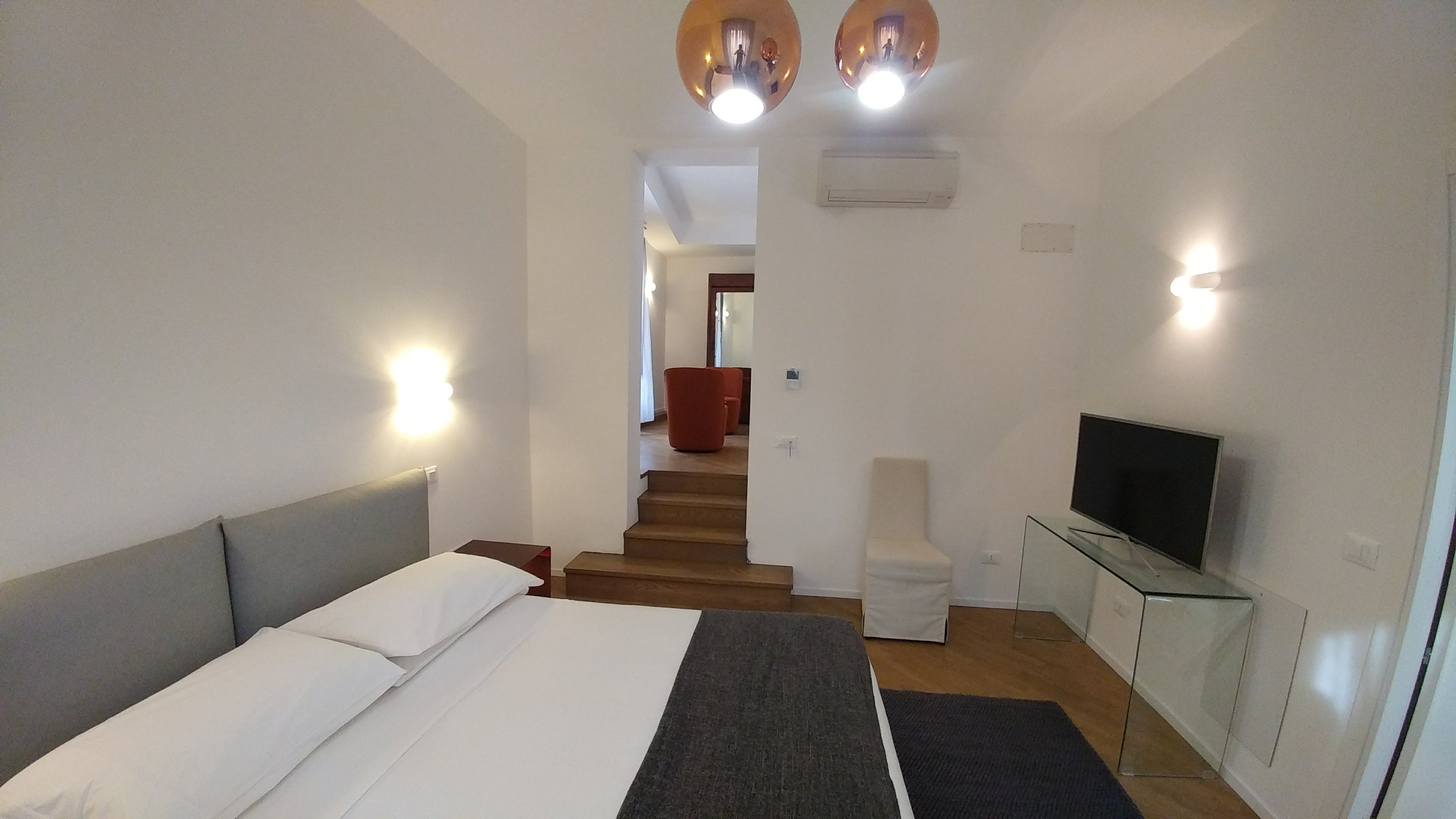 A modern hotel room with a bed, a TV, and a staircase leading to another room.