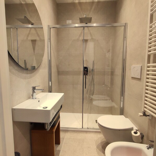 A modern bathroom with a glass-enclosed shower, a sink, a toilet, and a bidet.