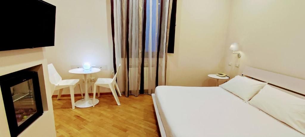A hotel room with a bed, a small table with chairs, a TV mounted on the wall, and a window with curtains.