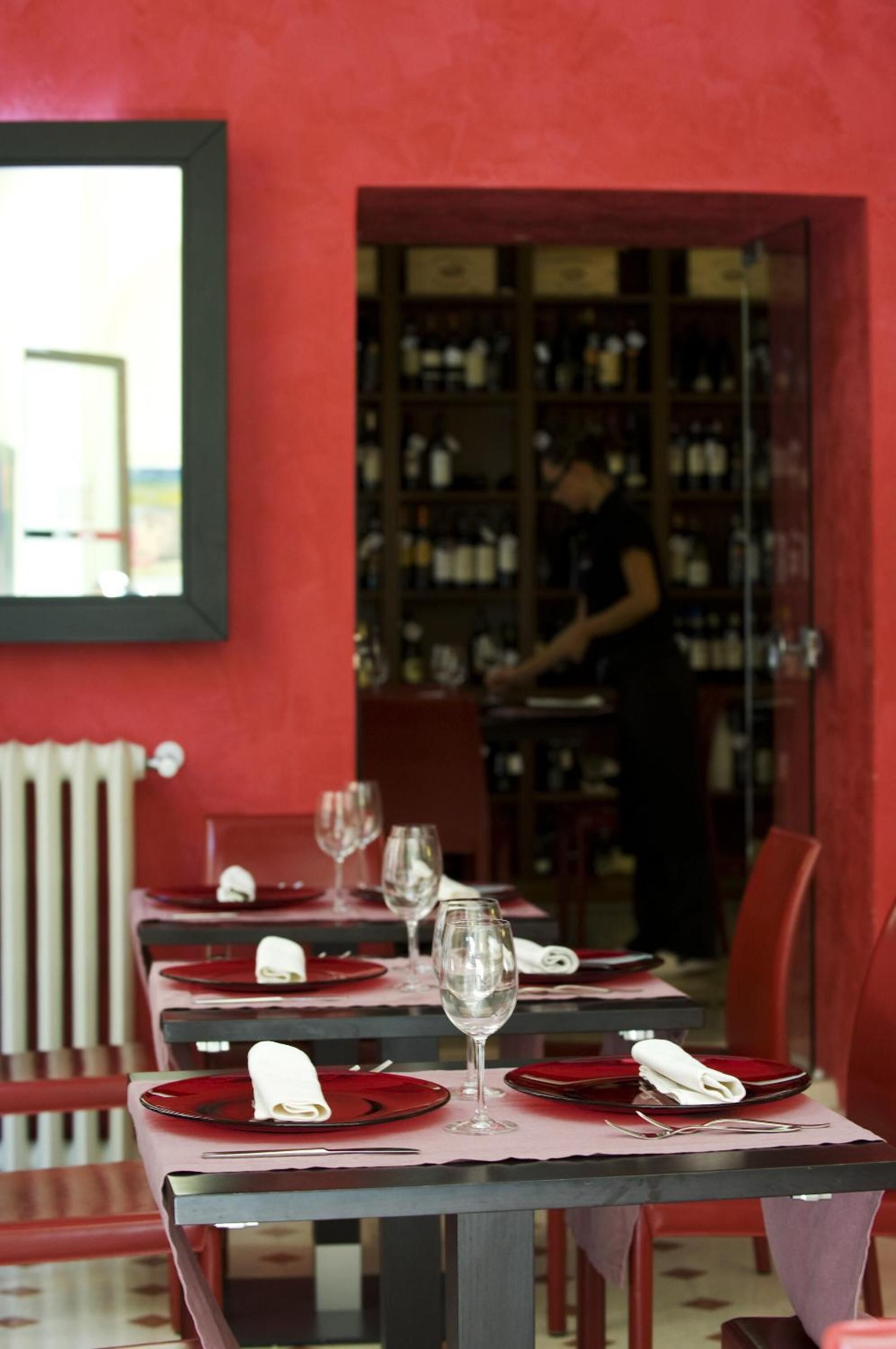 A restaurant with tables set for dining, a bartender in the background, and a wine rack.