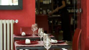 A restaurant with tables set for dining, a bartender in the background, and a wine rack.