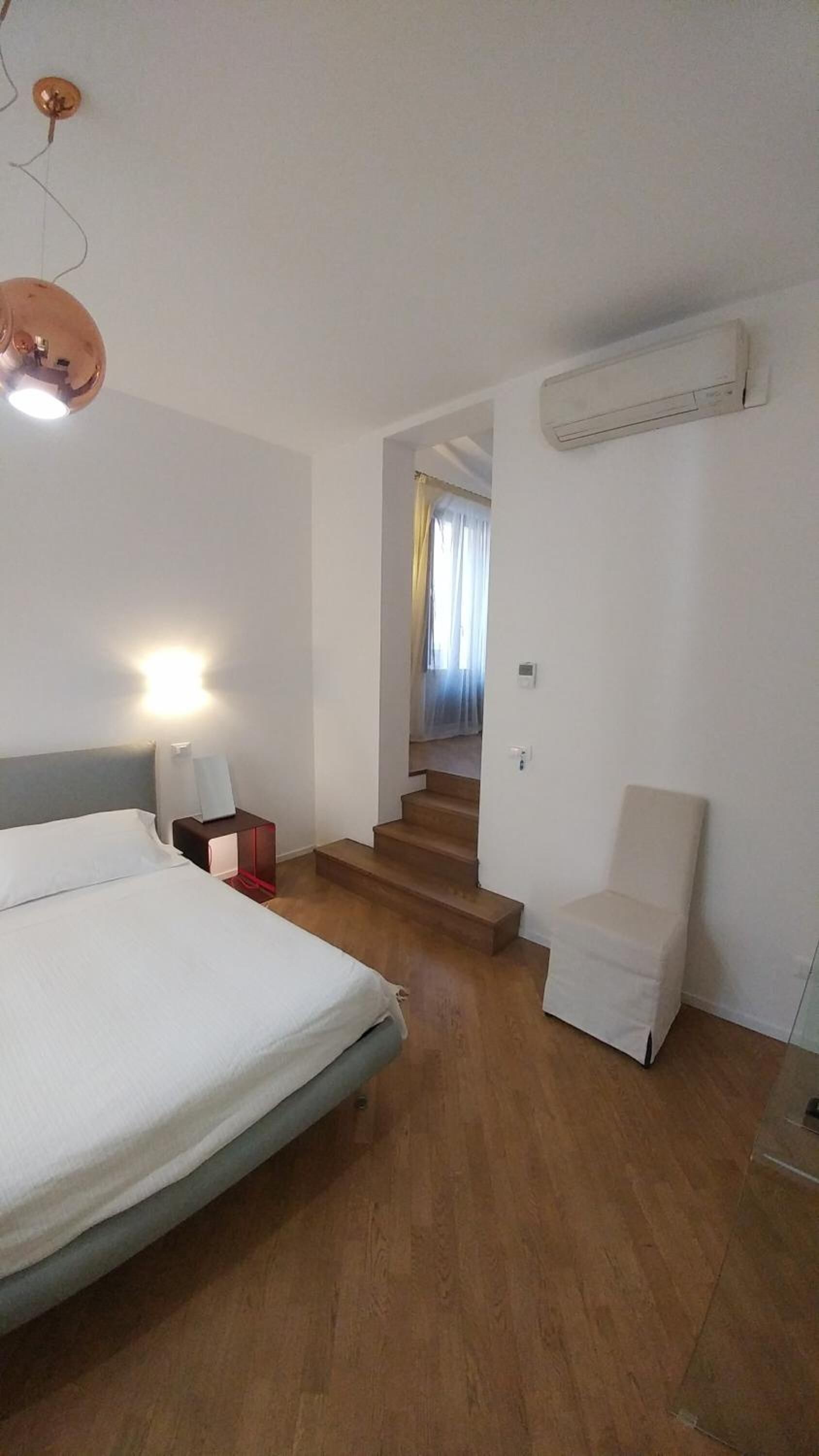Una habitación de hotel con una cama, una silla, una mesita de noche y una escalera que conduce a otra habitación.