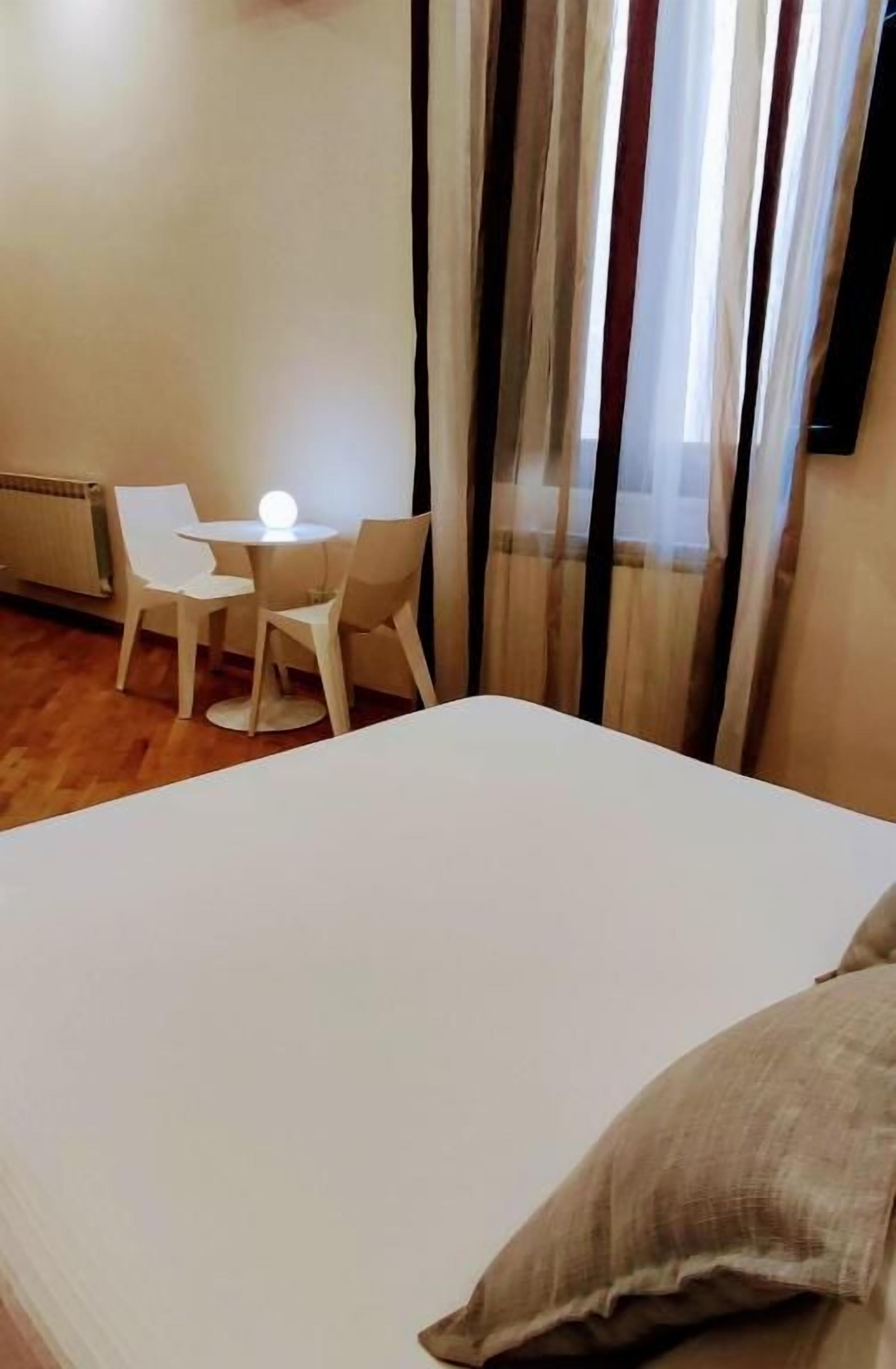 Una habitación de hotel con cama, una mesita con sillas y un ventanal con cortinas.