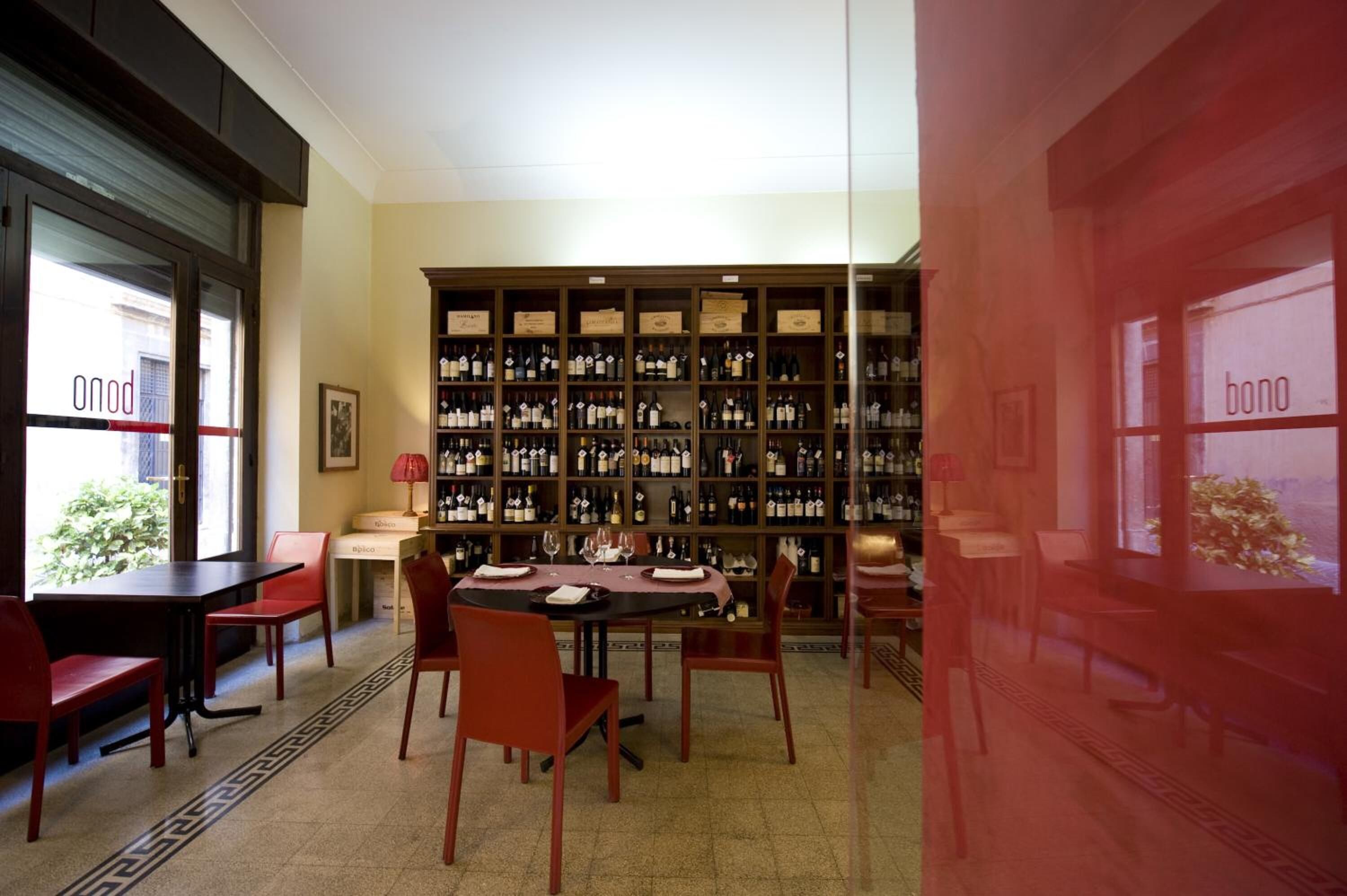 A dining area with a long table and red chairs, surrounded by a wine cellar with numerous bottles.