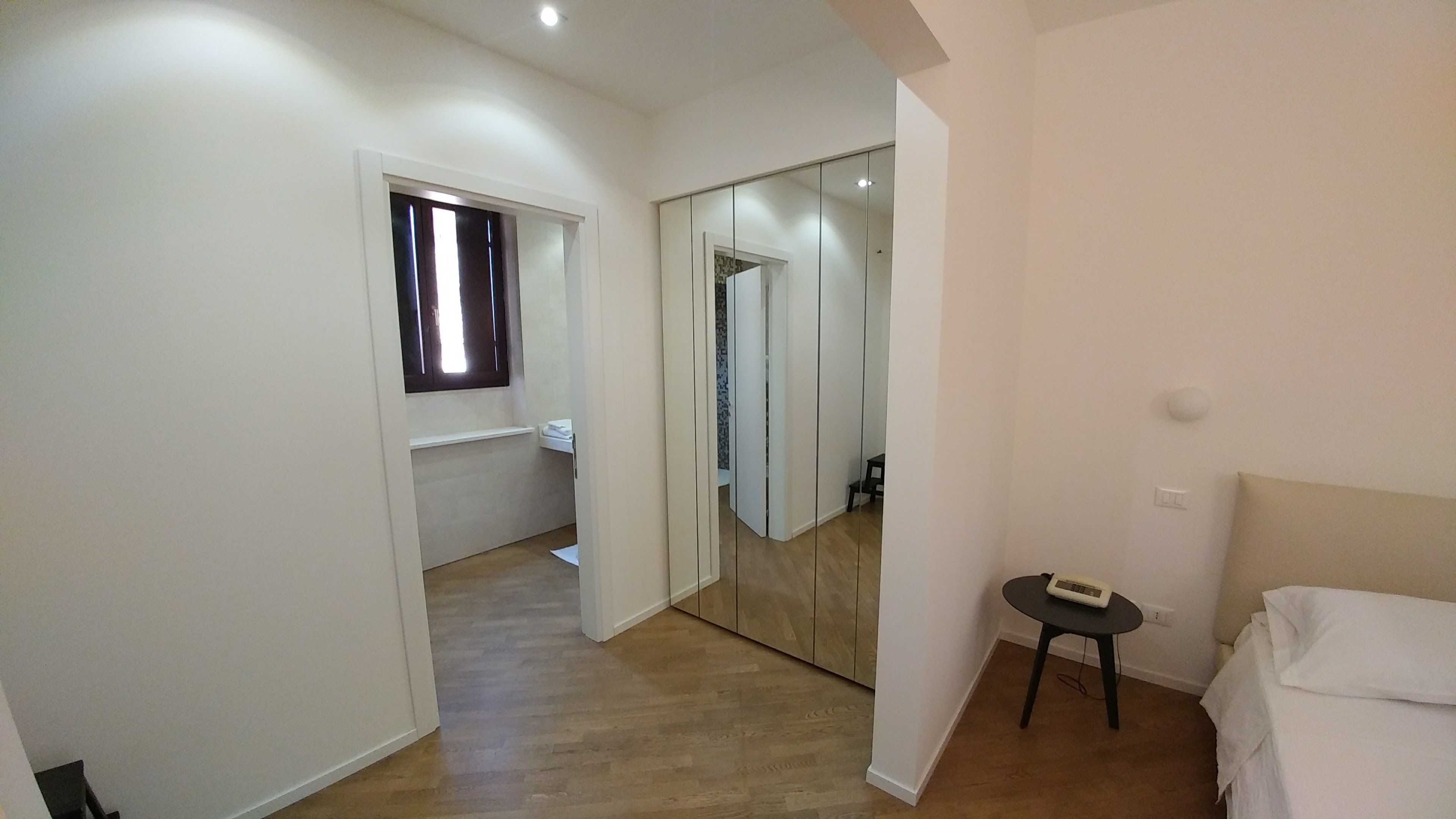 Un pasillo con suelo de madera que conduce a un dormitorio con cama y una mesita.