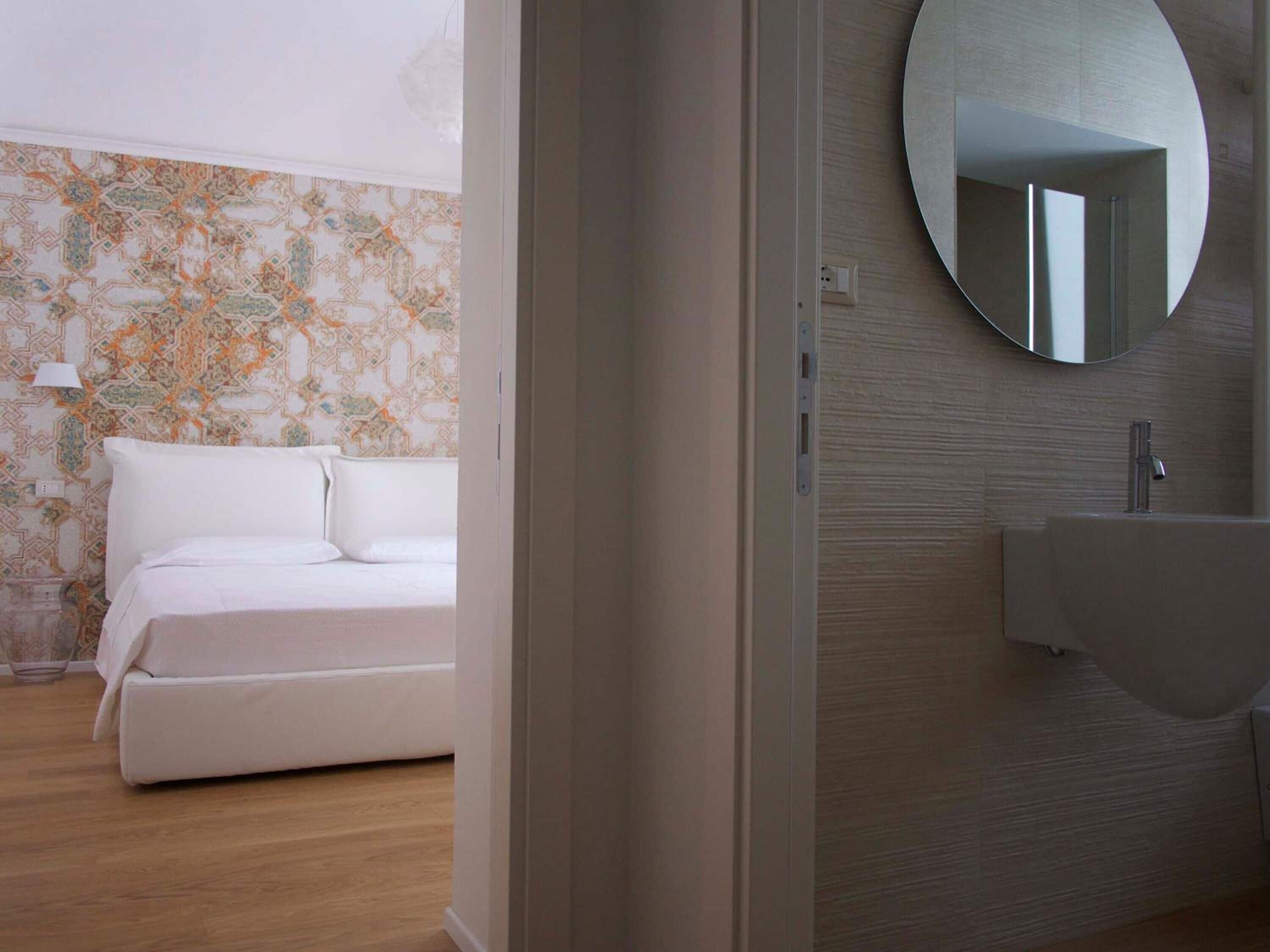 A modern hotel room with a bed, a round mirror, and a sink.