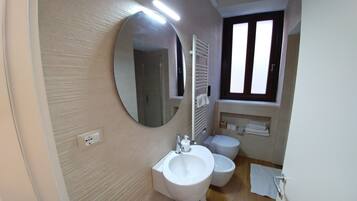 Un bagno con uno specchio grande, un lavandino, un water e una finestra.