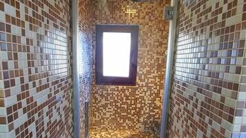A narrow bathroom with mosaic tile walls and a small window.