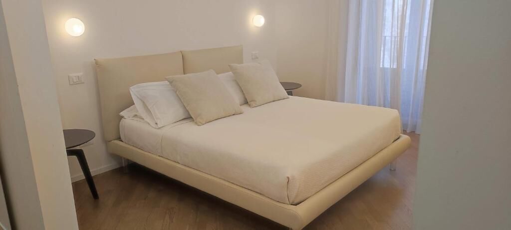 A bedroom with a bed, two bedside tables, and a window with sheer curtains.