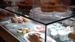 Vitrina de panadería con diversos pasteles y postres, incluyendo rosquillas y magdalenas, cubiertos por domos de plástico transparente.