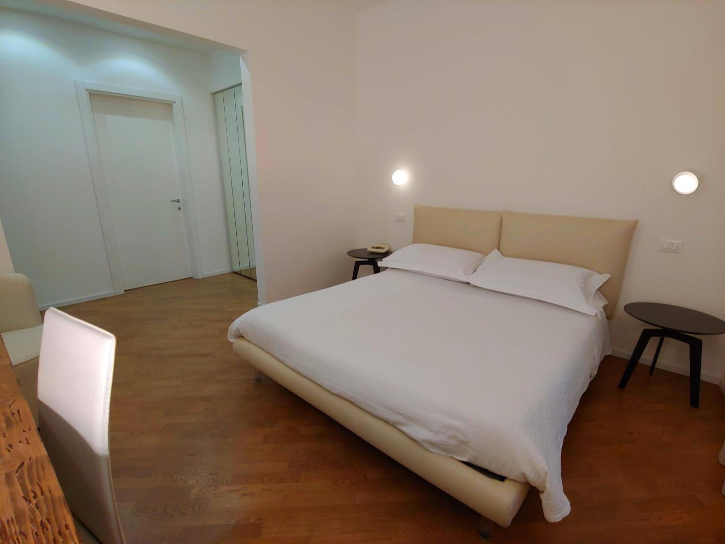 Een slaapkamer met een groot bed, nachtkastjes, een klein rond tafeltje en een deur naar een andere kamer.