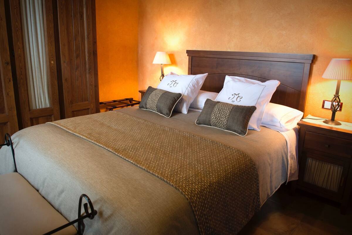 Una habitación de hotel con una cama grande, dos mesitas de noche y una ventana con cortinas.