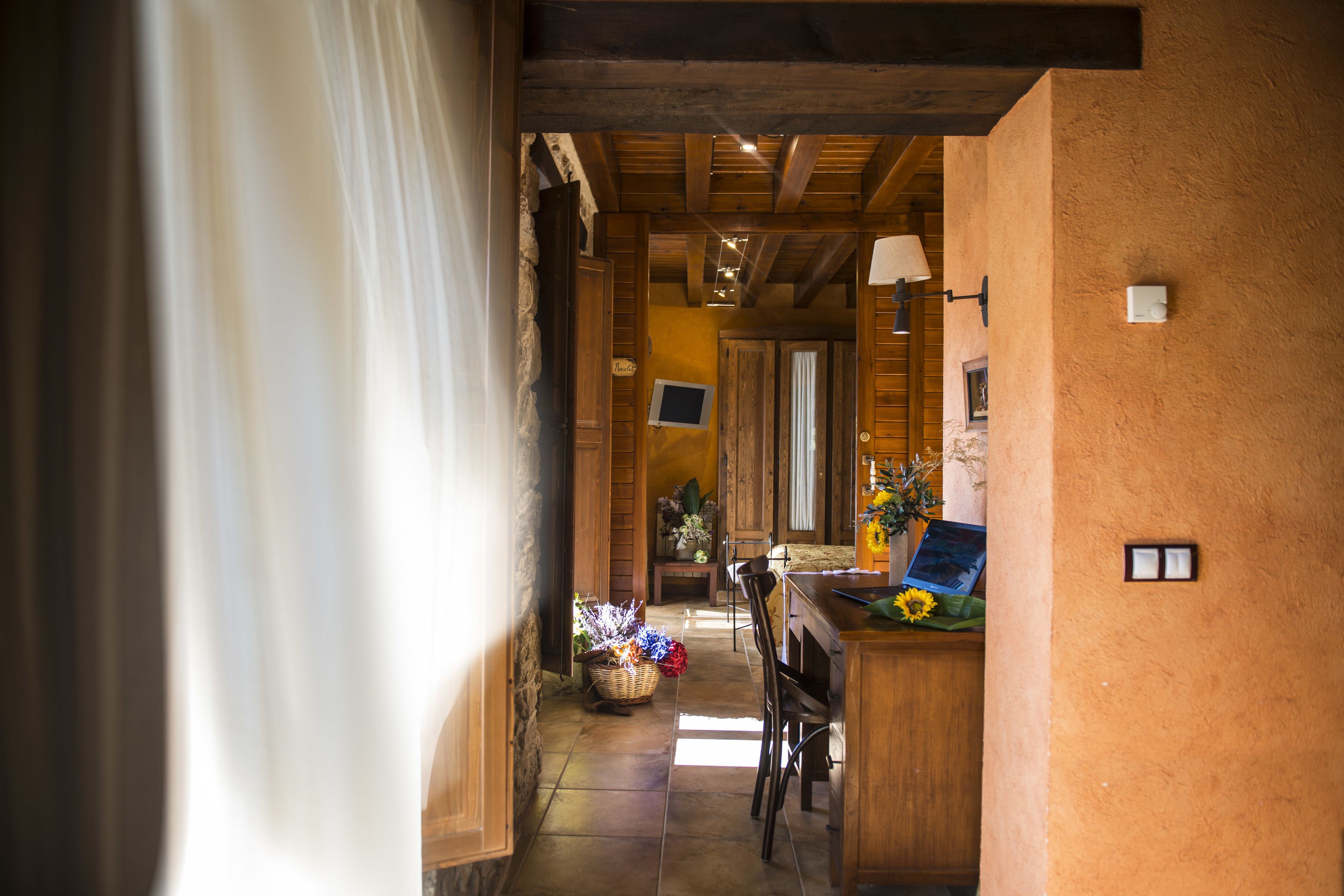 A hallway with wooden beams, a wicker basket with flowers, and a desk with a laptop and a vase of sunflowers.