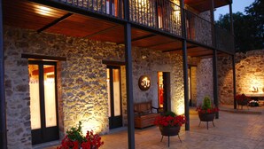 A stone building with a wooden balcony, potted red flowers, and a sign with a circular emblem. - Rusticae La Casassa de Ribes (Ribes De Freser)