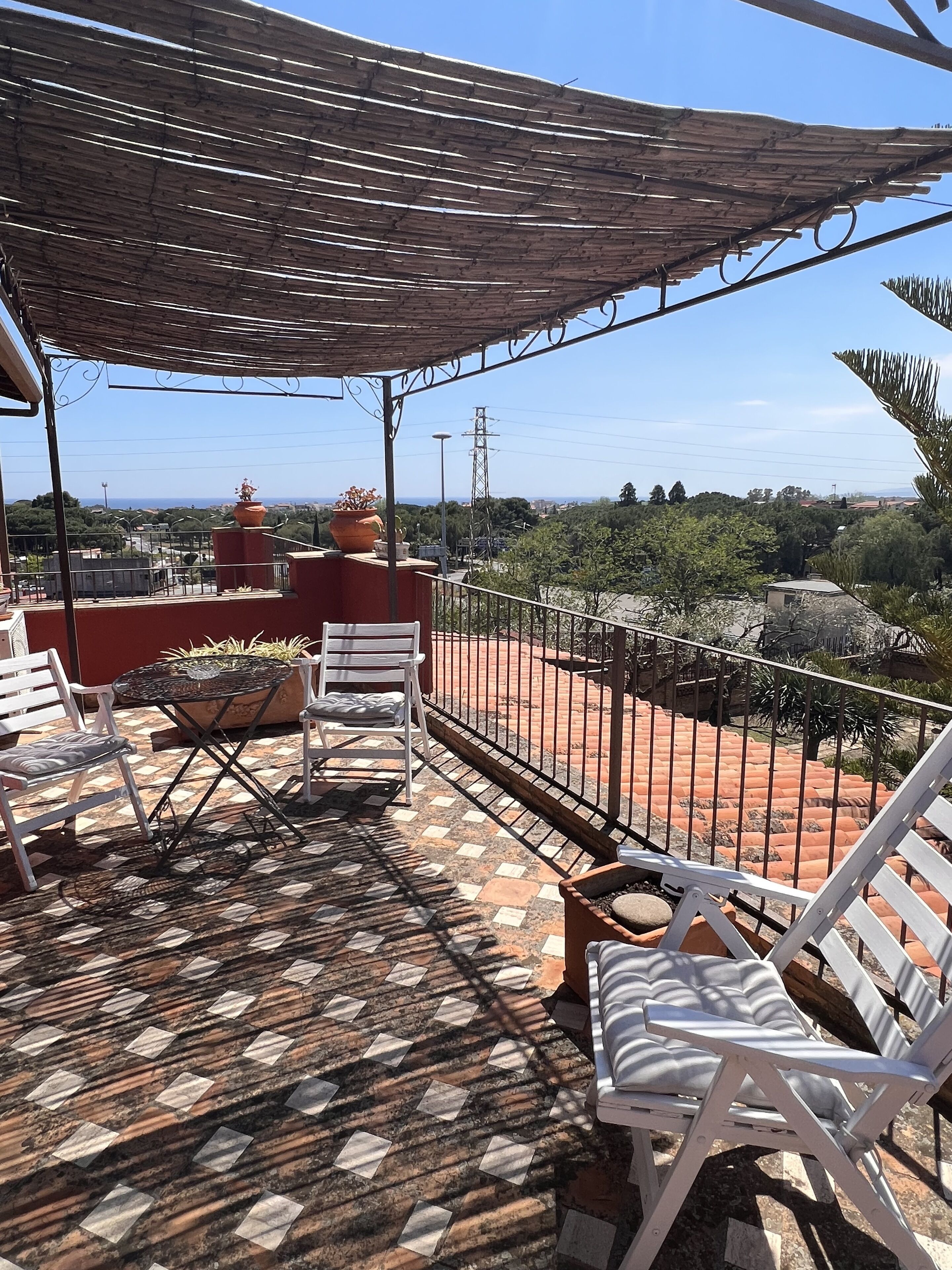 A terrace with a patterned floor, white chairs, a table, and a decorative pot.