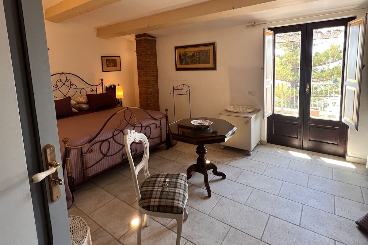 Un dormitorio con cama, una silla, una mesa y ventana con vistas.