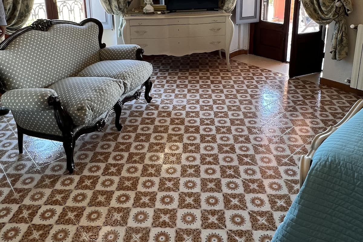 Una habitación con suelo estampado, un sofá, un televisor sobre un aparador y cortinas.