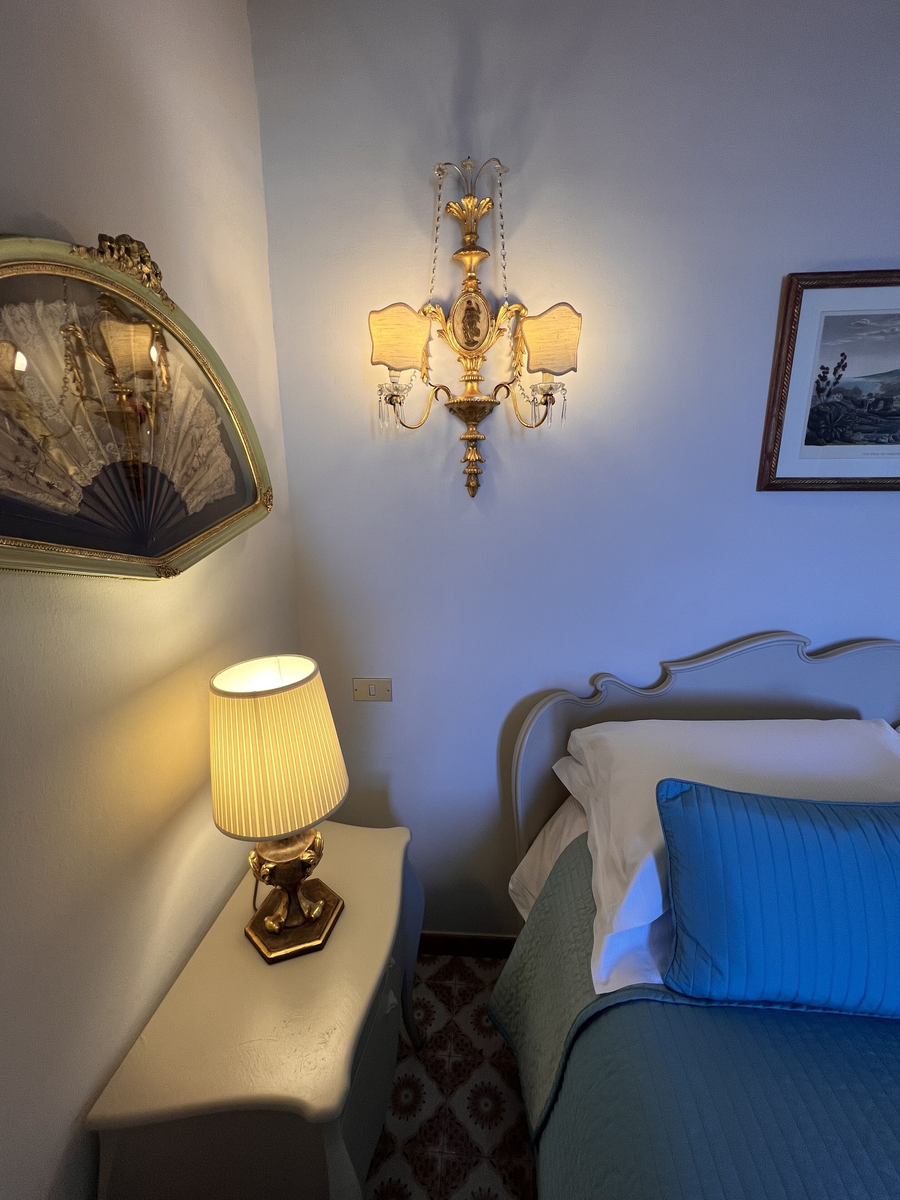 Ett hotellrum med en säng, en sänglampa, en väggmonterad lampa och en inramad tavla på väggen.