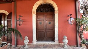 Entrada de un edificio con puerta de madera, piso de baldosas y dos faroles en las paredes.