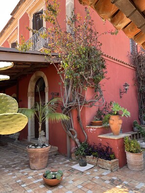 Une cour intérieure agrémentée de plantes en pot, d’un palmier et d’un bâtiment rouge doté d’un balcon.