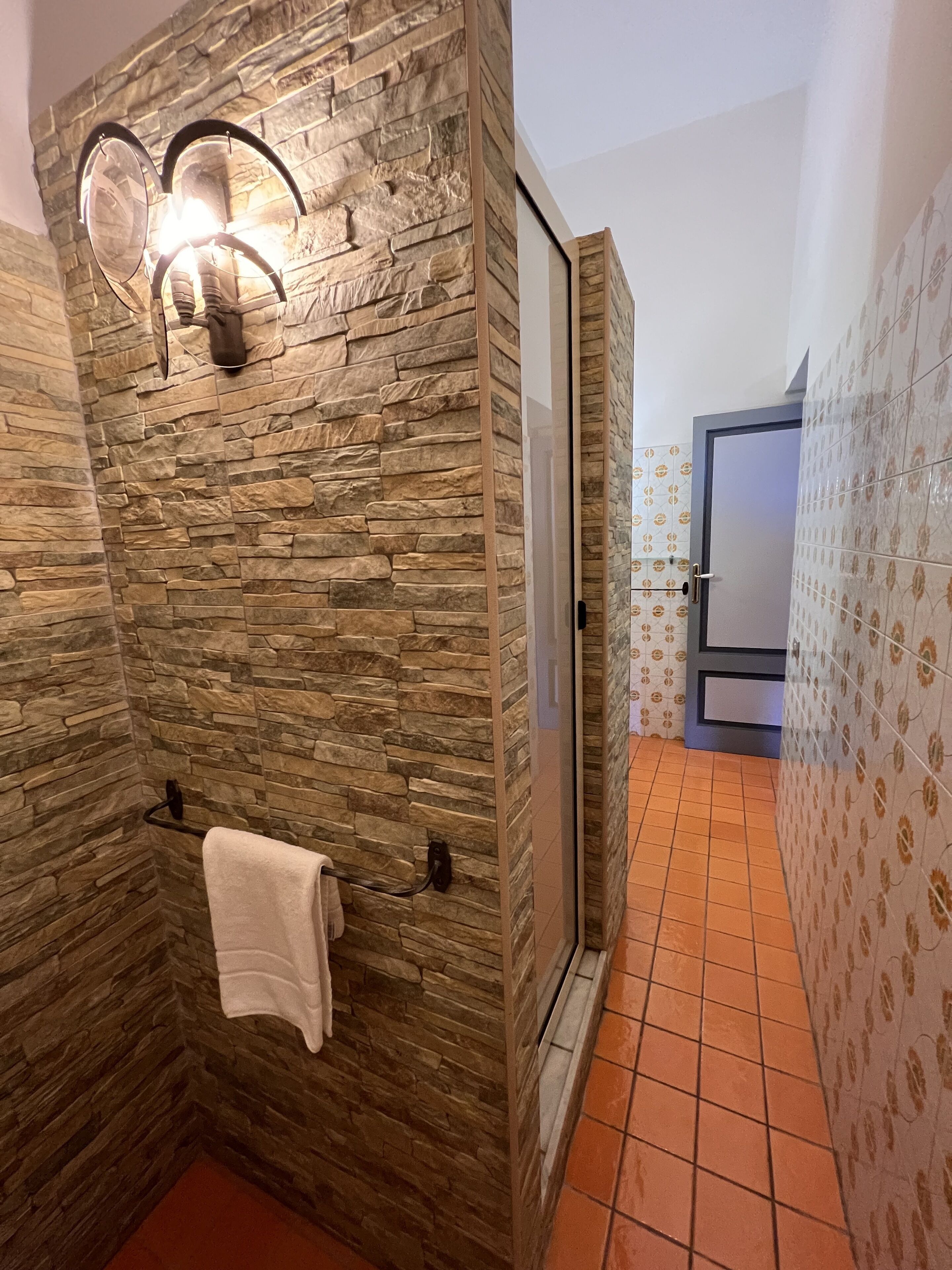 A bathroom with a stone wall, a glass shower enclosure, and patterned tiles.