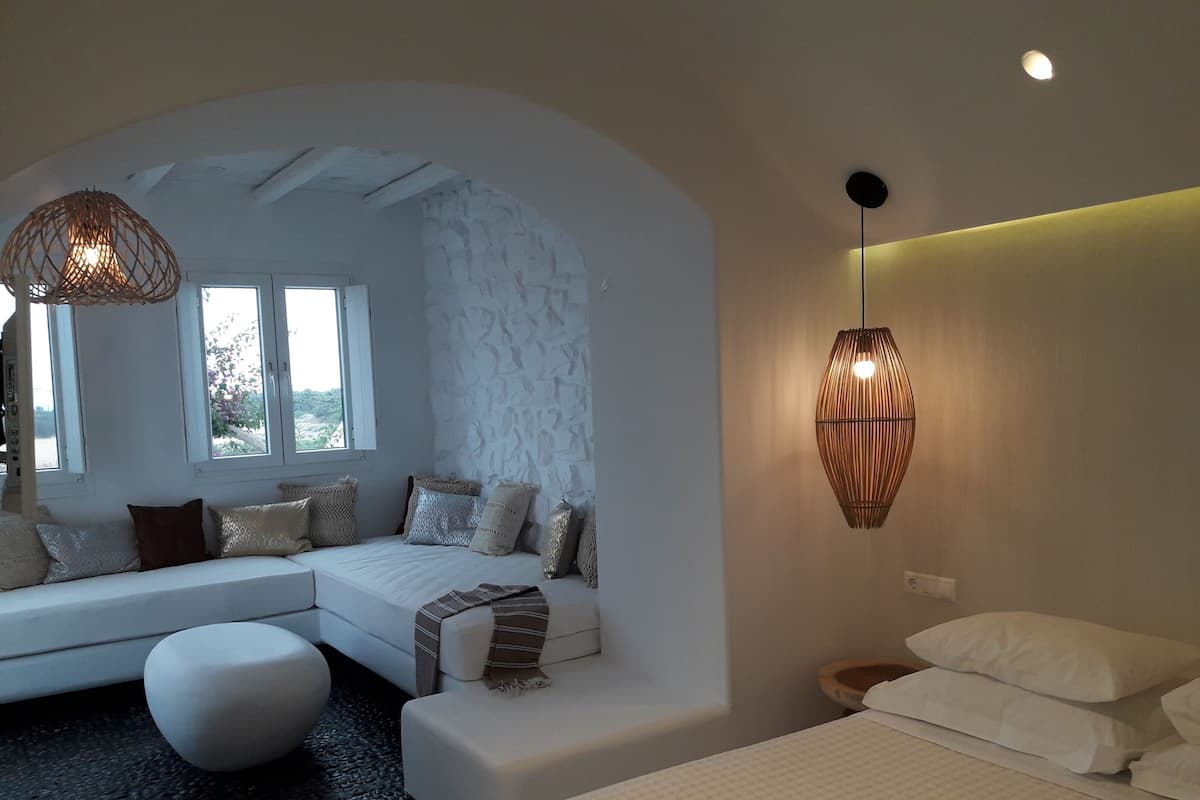 A modern bedroom with a curved ceiling, a large window, a sofa bed, a bedside table, and a wall-mounted lamp.