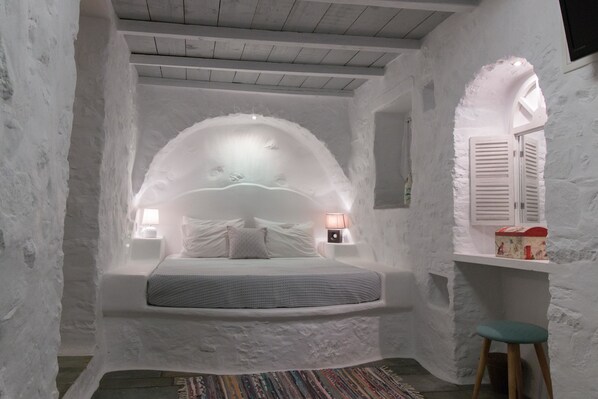 A cozy, white-themed bedroom with a built-in bed, a small desk, and a window with shutters.